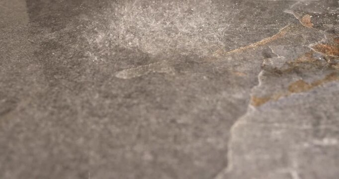 Slow motion water droplets on dark stone shower floor, close up footage captures instant falling spray strikes natural surface and scatters into delicate splash patterns in modern bathroom wet zone