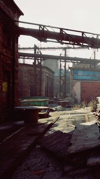 The scene shows an empty industrial area with old buildings and rusting machinery. Sunlight shines on the ground and highlights the worn structures. Overgrown plants add to the setting.