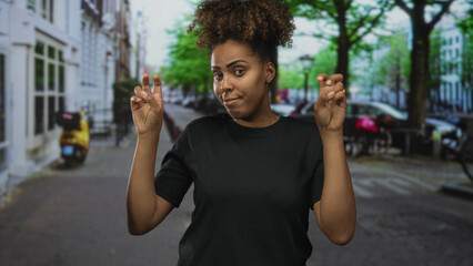 Naklejka premium Woman making air quotes with fingers on a city street, hands raised, wearing black tee and curly hair, face expressed with mild smirk; sarcasm commentary.