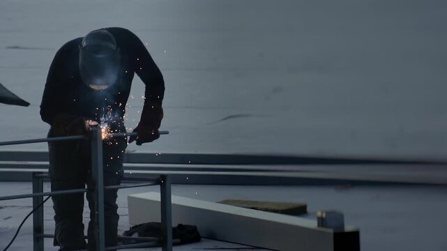 Professional welder performing intricate metal work, joining steel rods on rooftop construction site. Industrial process, hard work, safety. Slow motion x20. Protective gear worn, focused on task, spa