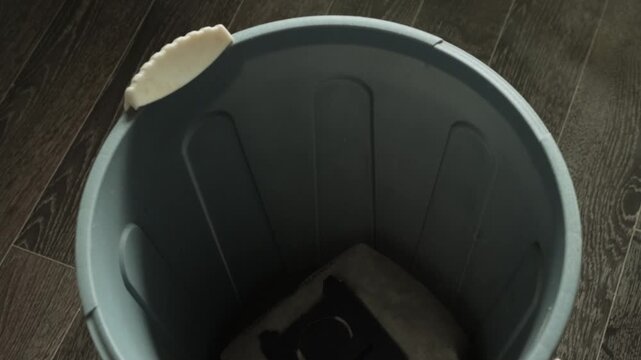 Detail shot of person hand replacing vacuum cleaner dust bag, removing old bag full of dirt and debris, placing bag into garbage bin, routine cleaning work, focus on efficient home upkeep.
