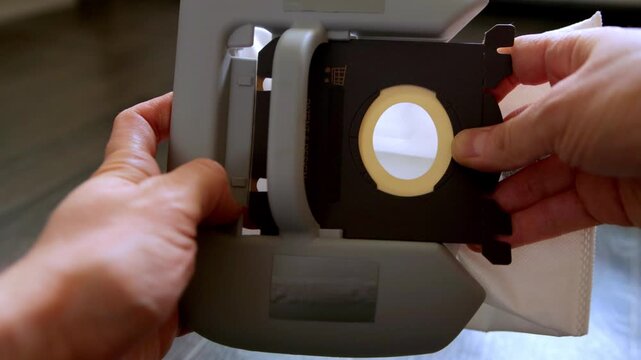 Close up view of person hands meticulously placing replacement dust bag into vacuum cleaner part, ensuring correct fit for optimal function of household cleaning equipment