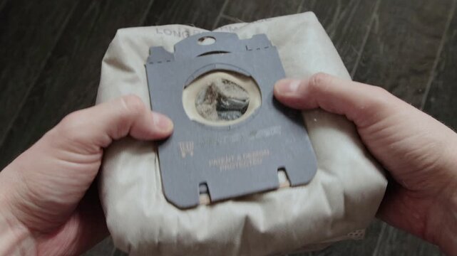 Close up view of hands holding vacuum cleaner dust bag filled with dirt, dust, and debris. Action demonstrates routine home maintenance, cleaning, and replacement process for appliance upkeep.