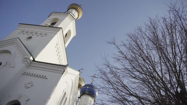 Low angle view of exterior of orthodox church building showcasing intricate details of white facade and vibrant golden bell tower dome contrasting with vivid blue domed structure.