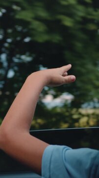 Back view. Happy child stretched out his hand from the car window. Boy waving hands gesturing out of the car window during a trip with his family. Slow motion.