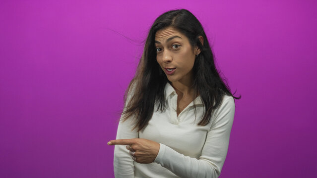 Woman pointing finger to left in studio with magenta wall and windblown hair; surprise playful curiosity.