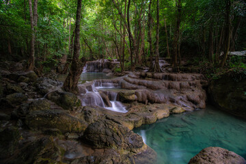 A turquoise waterfall cascades down in layers in the middle of the forest. © Pongsorn