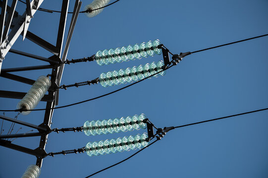 Close-up of electrical power transmission lines and insulators against a clear blue sky, showcasing energy infrastructure and utility poles