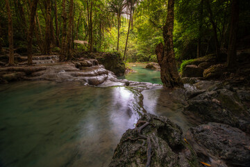 A turquoise waterfall cascades down in layers in the middle of the forest. © Pongsorn