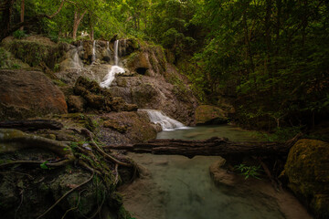 A turquoise waterfall cascades down in layers in the middle of the forest. © Pongsorn