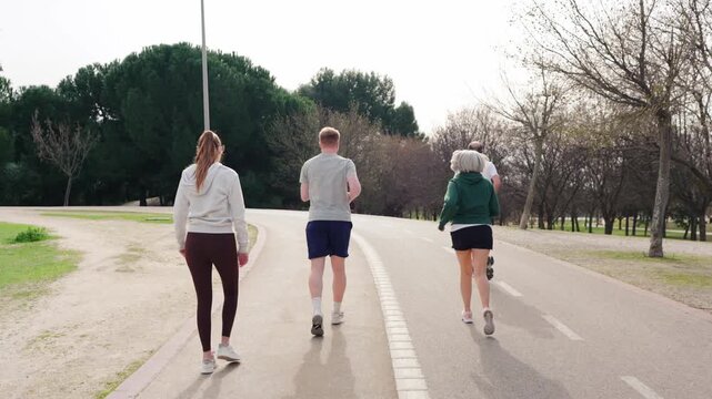 Four friends, two men and two women, jogging and walking together on a paved path in a park. Outdoor activity for a healthy lifestyle