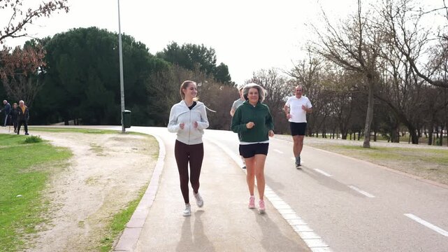 Mixed age group of people running together on a paved path in a public park. Active friends enjoying a healthy lifestyle outdoors