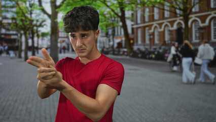 Fototapeta premium Man points finger like a gun on city street with bare hands and forearm visible; playful mock gesture.