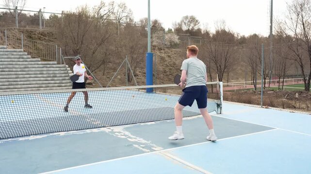 Two male friends enjoying a friendly yet competitive game of pickleball on a sunny day. Young athletes having fun during a rally on an outdoor court