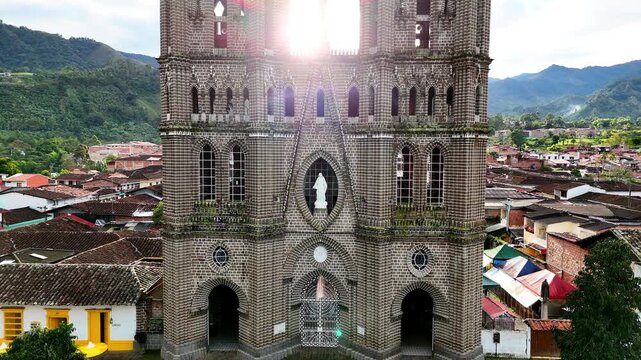A cinematic drone shot of the Basilica Menor in Jard&iacute;n. Starting at the spires with the sunrise behind, the camera moves downward to reveal the stone facade.