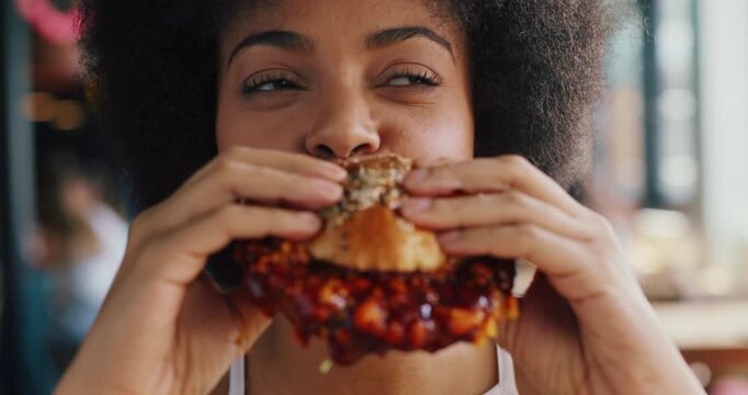 Happy, woman and burger in restaurant with delicious taste, sauce and eating fast food for lunch. Hungry, African person or customer in diner with beef sandwich, take away or meal for unhealthy diet.