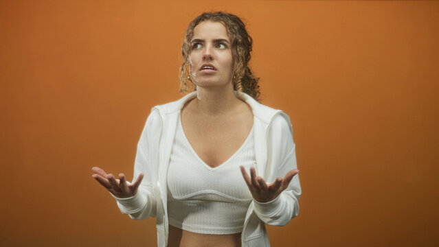 Young woman in white hoodie and crop top, open palms pleading and looking upward in studio; frustration yearning.