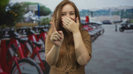Fototapeta premium Woman clasps hands before row of red rental bikes parked at busy downtown street corner; anticipation.