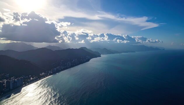 Ocean view of a skyline with buildings lining the coast under a sunlit blue sky filled with dramatic clouds
