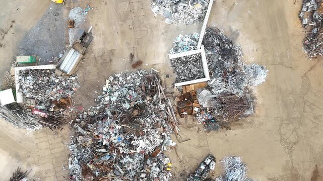 Aerial view of waste sorting and recycling process at a garbage facility, showcasing piles of scrap metal, debris, and machinery in a large outdoor area