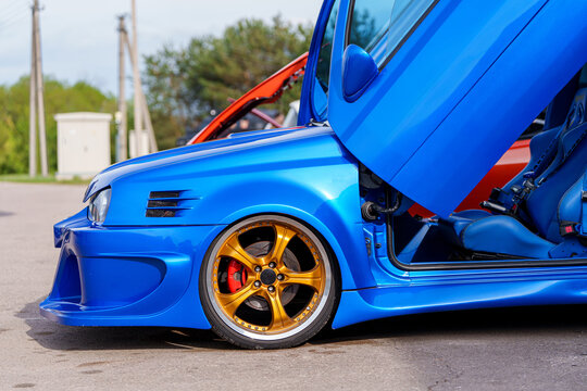 Side profile of a modified blue Volkswagen Golf with vertical scissor doors, gold alloy rims, and wide body kit, custom automotive tuning and aftermarket styling