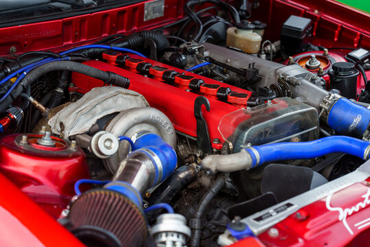Angle view of a modified sports car engine bay featuring a 1JZ inline-six engine, large aftermarket turbocharger, red cam covers, and blue silicone intercooler piping