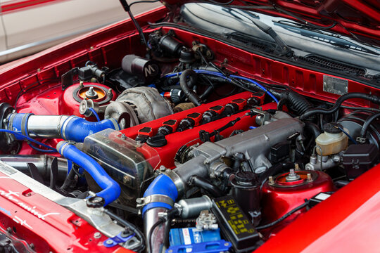 Angle view of a modified sports car engine bay featuring a 1JZ inline-six engine, large aftermarket turbocharger, red cam covers, and blue silicone intercooler piping