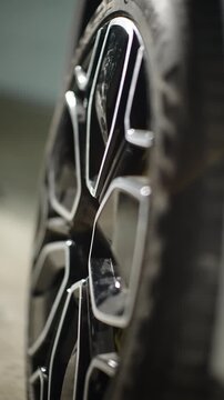 Close-up of a gloved mechanic tightening a lug nut with a torque wrench on a sleek black alloy wheel, showcasing precision automotive maintenance and modern geometric rim design.
