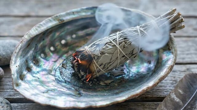 Sage bundle smoking in an abalone shell with wisps of smoke rising gracefully. This sage bundle smoking ritual creates a serene atmosphere, enhancing mindfulness and tranquility.