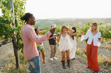 Naklejka premium Multiracial friends dancing at summer party inside vineyards - Happy people having fun together during wine taste event - Travel and celebration concept - Focus on right blond girl face