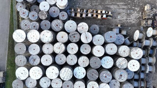 Aerial view of wooden cable spools arranged in a grid pattern on the ground, showcasing the varying sizes and orientations of the spools in a storage area
