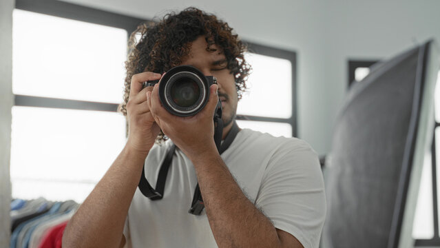 Young indian man photographer holding camera to eye with hand on shutter in studio; concentration creativity.