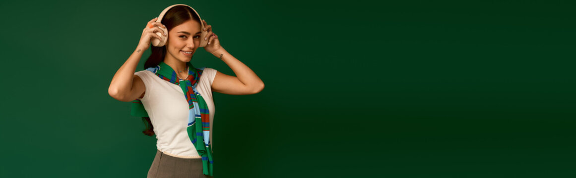 Stylish young woman in trendy outfit poses with headphones in vibrant green studio