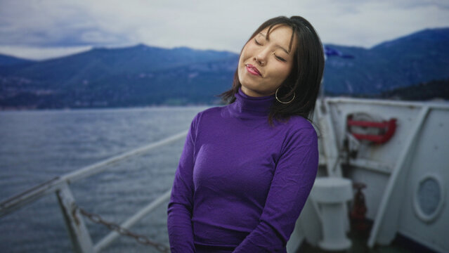 Woman smiling with face tilted, wearing purple turtleneck on boat near forest shore and deck railing visible; carefree joy.