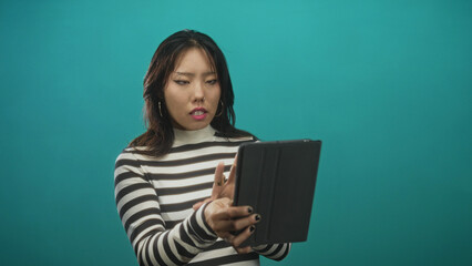 Naklejka premium Woman in striped sweater holding tablet, fingers tapping and gesturing toward screen while studying content in studio; concentration learning engagement productivity.