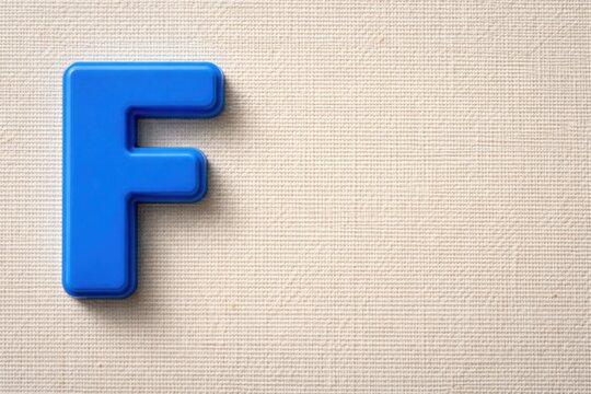 Textured canvas background with bold blue plastic letter F and blank copy space