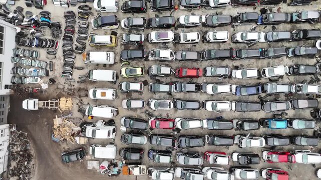 Aerial perspective of a car junkyard filled with numerous dismantled vehicles, displaying a variety of colors and models, with visible scrap materials and parts
