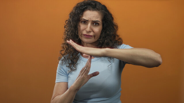 Woman wearing blue shirt frowning makes timeout gesture with hands in orange studio; pause break frustration.