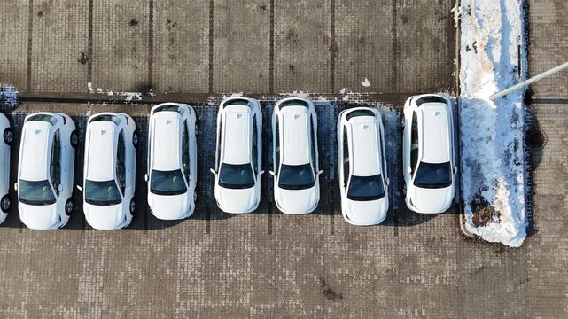 Aerial view of multiple new white cars parked in a straight line on a snow-covered parking lot at a car dealership, commercial auto showroom display, brand new vehicles for sale, modern automotive ret