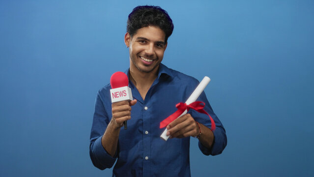 Man holding a red microphone, smiling and presenting a ribboned diploma toward camera in studio; pride success.