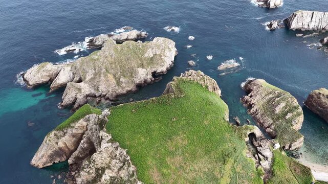 Aerial view of Silence Beach featuring rugged cliffs with green plateaus and rocky islets surrounded by turquoise waters in Asturias, Asturias, Spain.