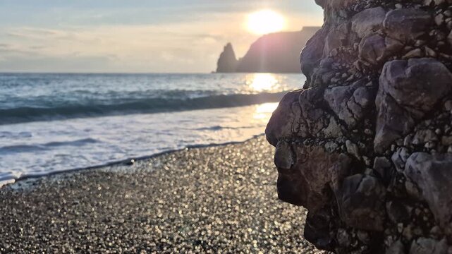 Sunset beach rocks gentle waves crashing on a pebble shore with a textured foreground rock in a peaceful coastal landscape