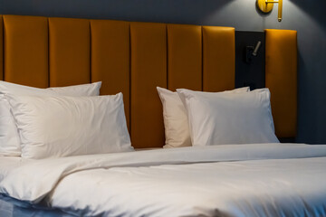 Freshly made hotel bed with white linens, pillows, and a duvet. Dim warm lighting. Wall-mounted bedside lamps on. Gray walls, orange upholstered headboard. Cozy elegant interior. © magpie