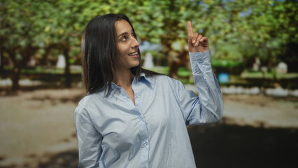 Fototapeta premium Woman showing ok sign with fingers and smiling in forest setting wearing light blue shirt; joy approval.