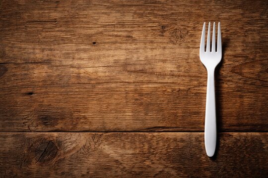 White plastic fork set on rough wooden plank table with copy space