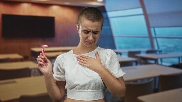 Woman holds pink razor in one hand, other hand on chest, grimacing and inspecting in building; disgust hesitation.