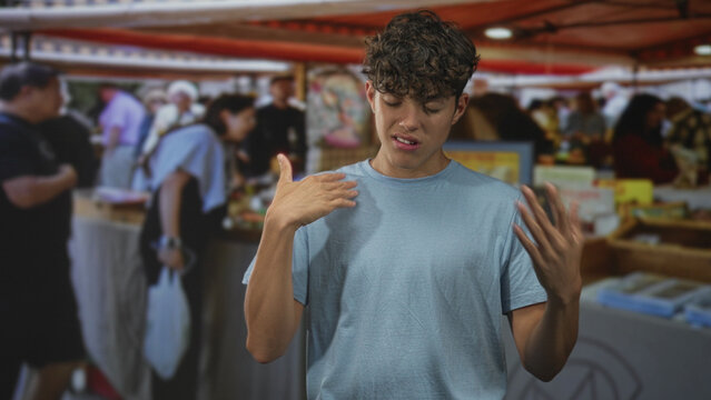 Man smoothing shirt and gesturing with both hands amid crowded street market stalls and vendors; frustration doubt.