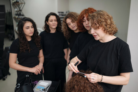 Professional hairdresser instructor teaching students biowave and permanent curling techniques using perm rods on a mannequin head during a beauty school masterclass.
