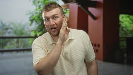 Fototapeta premium Man cups hand to ear in building, leaning forward with visible hand and face, listening gesture; surprise curiosity.