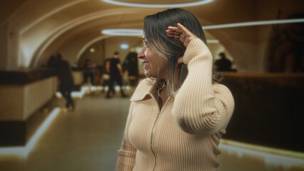 Hispanic woman shading eyes with hand at hotel reception counter wearing beige zip sweater and necklace  calm travel. © Krakenimages.com